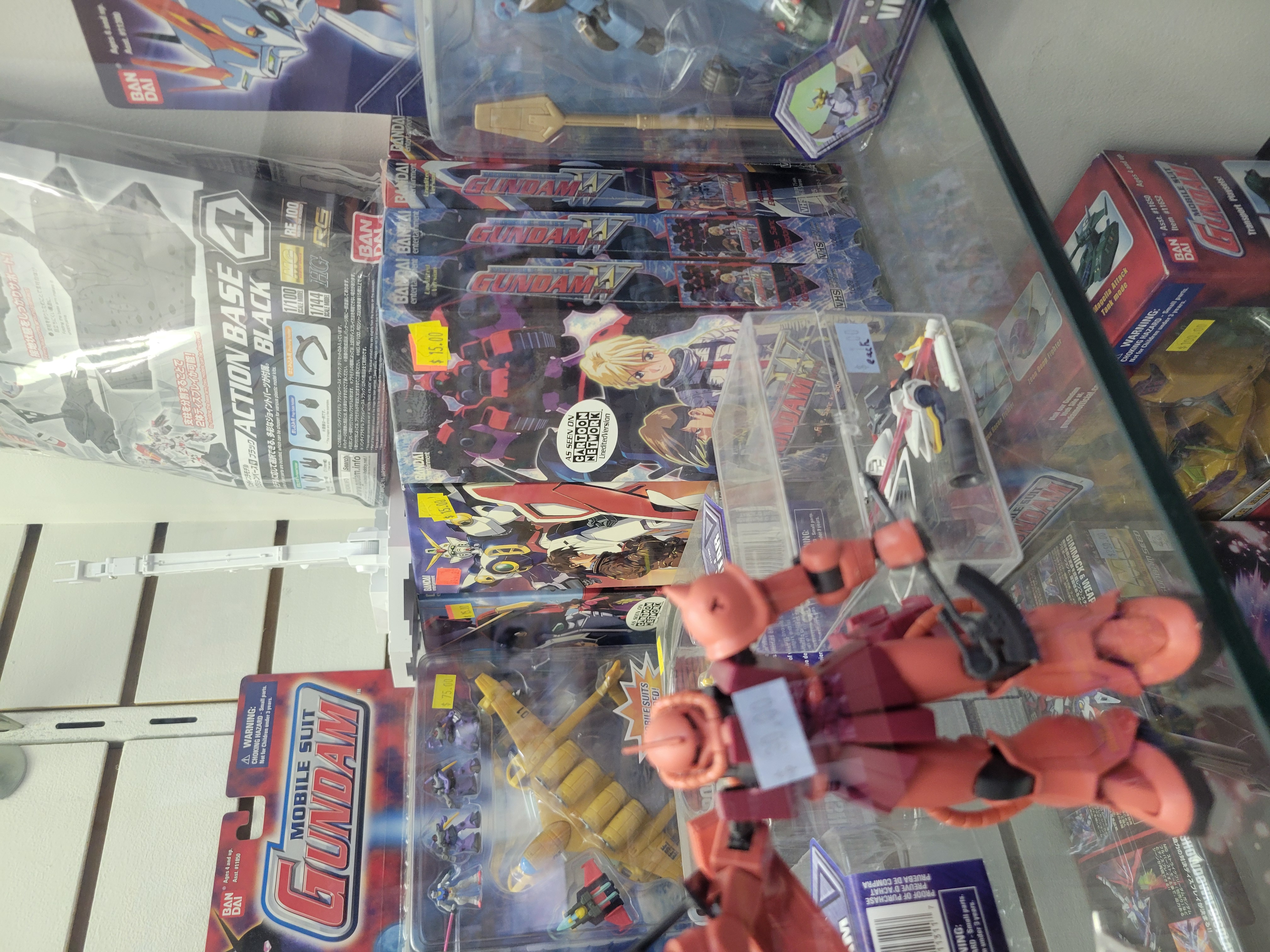 Glass case filled with toys from various Gundams series and Gundam Wing video tapes.